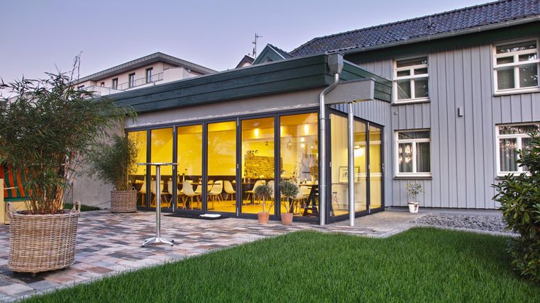 Een moderne uitbreiding met grote ramen en een gezellige binnenruimte. De tuin is goed onderhouden met groen gras en planten.