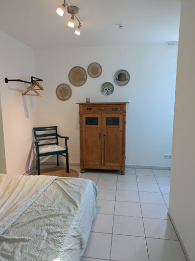 Een eenvoudig ingericht vertrek met een bed en een houten kast. Aan de muur hangen decoratieve borden en er staat een stoel in de hoek.