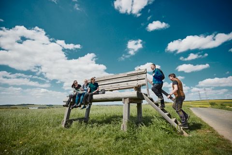 Die XXL-Bank auf einer grünen Wiese in Möntenich. Drei Menschen sitzen bereits auf der Bank und zwei weitere steigen über die Treppe auf die Bank.