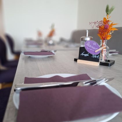 Une belle table dressée dans un restaurant avec des serviettes violettes et un petit bouquet de fleurs. Sur la table se trouve un panneau avec "Réservé" et le prix de 35,50 €.