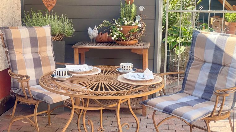 Een gezellige buitenruimte met een ronde tafel en twee comfortabele stoelen. Daarnaast is er een ligbed en een parasol.