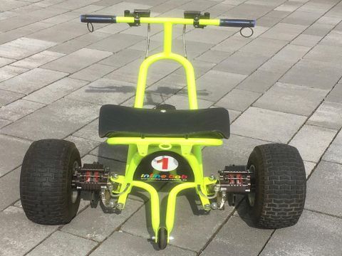 Une voiture à pédales jaune vif et noire avec de grands pneus est posée sur un sol pavé. Le véhicule semble destiné aux enfants pour jouer.