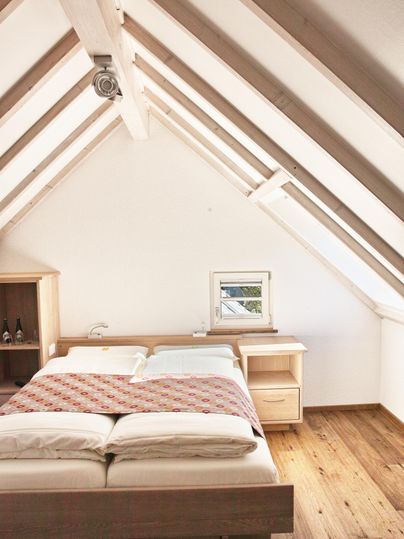 Een gezellige slaapkamer met een groot bed en een houten vloer. Het plafond heeft een moderne dakconstructie met zichtbare balken.