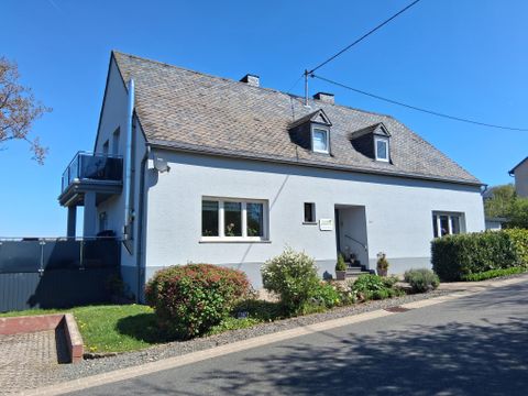 Een helder, twee verdiepingen tellend huis met een grijze gevel en een zadeldak. De tuin is verzorgd en er is een wandelpad voor het huis.