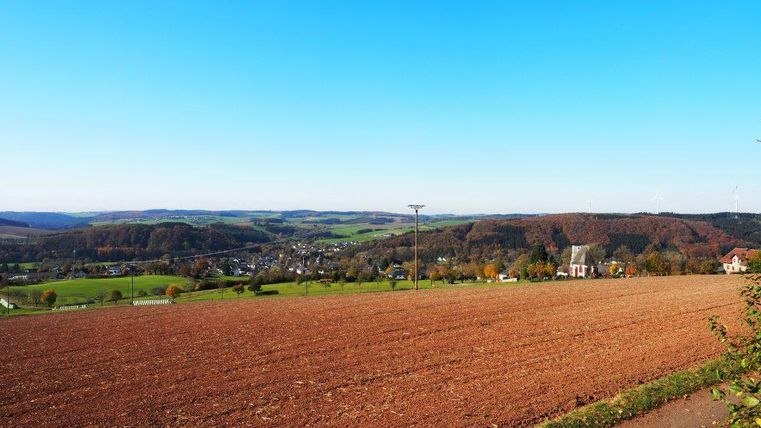 Een wijd landschap met een akker op de voorgrond en glooiende heuvels op de achtergrond. De lucht is helder en blauw, ideaal voor een zonnige dag.