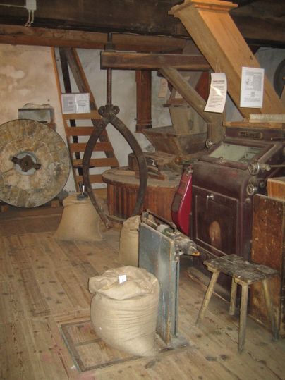 Innenansicht einer historischen Mühle mit Mühlsteinen, Säcken und Holzkonstruktionen.