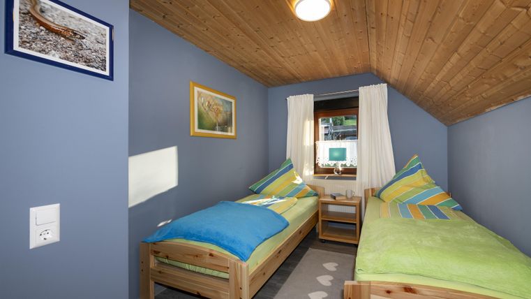 Een gezellige slaapkamer met twee eenpersoonsbedden, kleurrijke dekbedden en houten plafonds. Aan de muren hangen schilderijen, en het licht stroomt door de ramen.