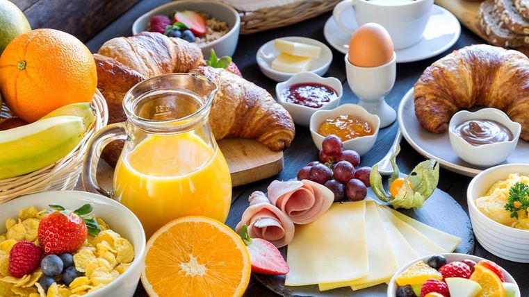 Un petit-déjeuner copieux avec des fruits frais, des croissants et des céréales. Il y a aussi du jus d'orange et du café sur la table.