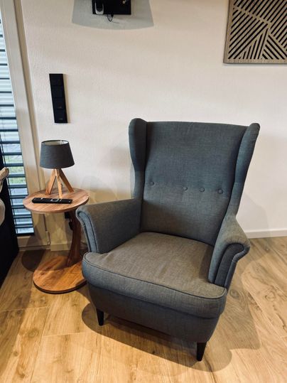 A gray armchair with a high back is situated in a modern room. Next to the armchair is a small table with a lamp.