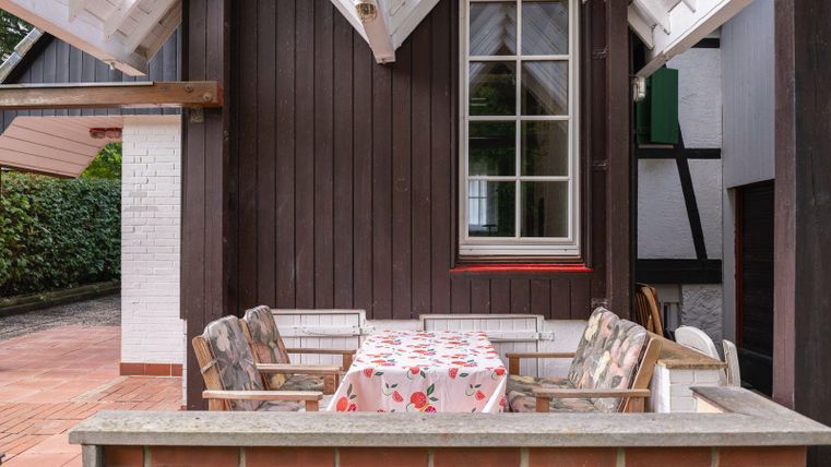 Un espace extérieur confortable avec une table et des chaises. La table a une nappe fleurie et est entourée d'un mur simple.