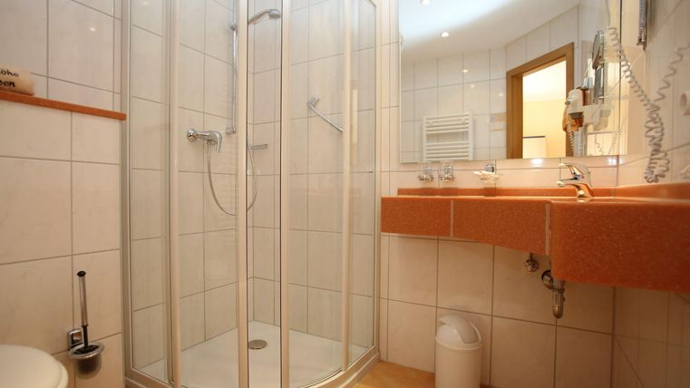 Een moderne badkamer met een douchecabine en lichte tegels. Het wasgedeelte heeft een grote spiegel en een praktische plank.