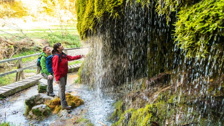 Twee mensen staan onder een met mos bedekte waterval.