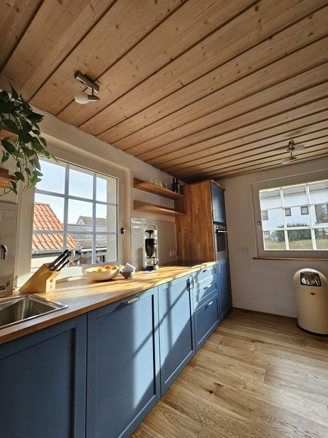 Een moderne keuken met blauwe kasten en houtaccenten. Het licht valt door de ramen en zorgt voor een uitnodigende sfeer.
