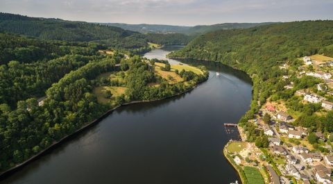 Luftaufnahme eines Flusses in einem bewaldeten Tal mit einem Dorf am Ufer.