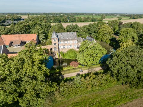 Aerial view of a castle with moat, surrounded by trees and fields.