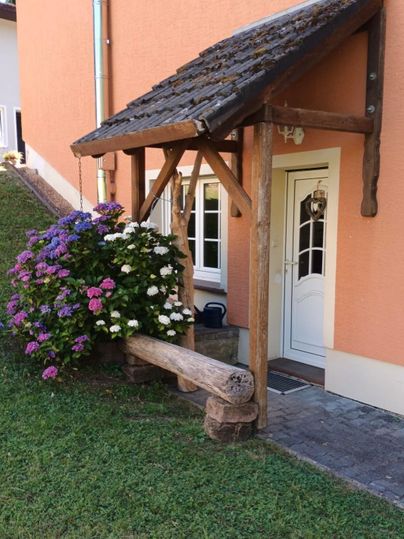 Ein hübscher Eingangsbereich mit einem überdachten Vorbau aus Holz. Bunte Hortensien blühen neben der Tür und verleihen dem Haus einen einladenden Charme.