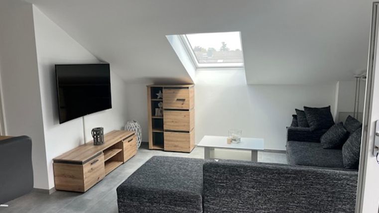 Un salon moderne avec un canapé confortable et une grande télévision. La pièce a des murs clairs et beaucoup de lumière naturelle grâce à la fenêtre de toit.