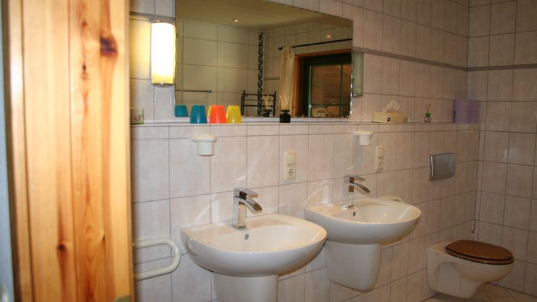 Een moderne badkamer met twee wastafels en een grote spiegel. De ruimte heeft lichte tegels en een aangename verlichting.