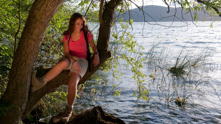 Frau sitzt auf einem Baum am Ufer des Laacher Sees.