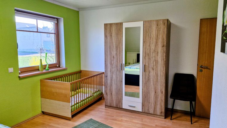Een lichte kinderkamer met groen geschilderde muren. De kamer bevat een wieg, een kast en een stoel.