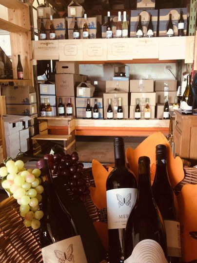 Een wijnwinkel met meerdere rekken gevuld met wijnflessen. Op de voorgrond staan enkele wijnflessen en druiven.