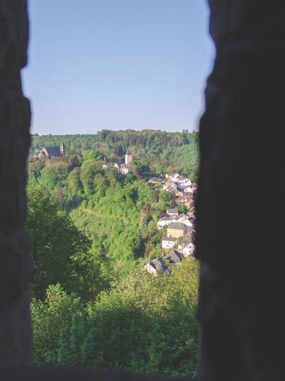 Vue sur un paysage verdoyant avec une église et des maisons, encadrées par des silhouettes sombres.