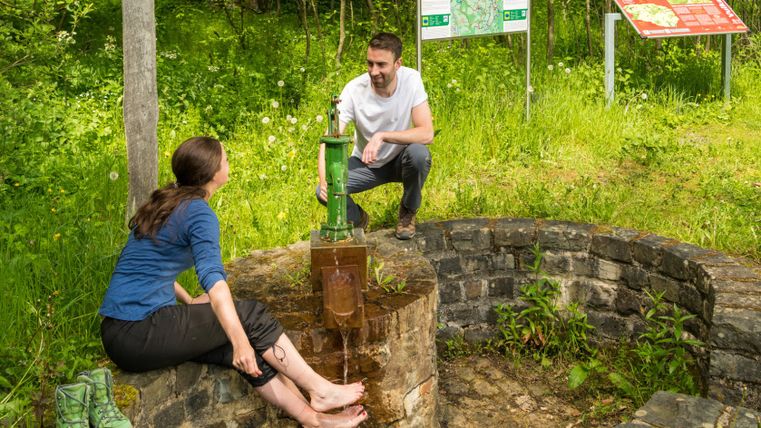 Deux personnes au Demerather Drees sur le sentier Vulcano, l'une se rafraîchit les pieds dans l'eau.