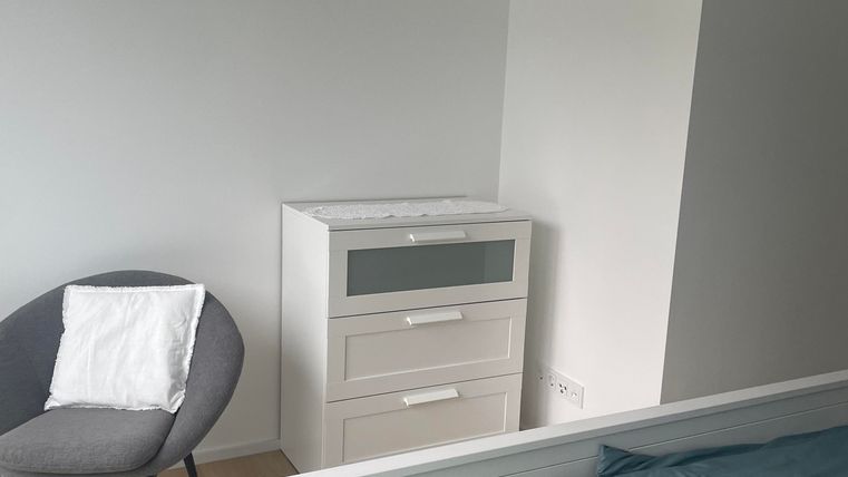 Ein Schlafzimmer mit einem weißen Bett und einem modernen Nachttisch. Ein grauer Stuhl steht neben dem Bett.