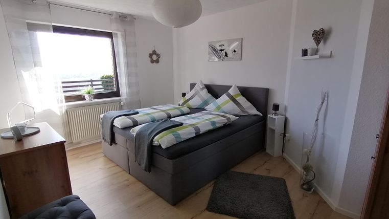 Ein gemütliches Schlafzimmer mit einem großen Doppelbett und bunten Kissen. Der Raum ist hell und freundlich, mit einem Fenster, das für Tageslicht sorgt.