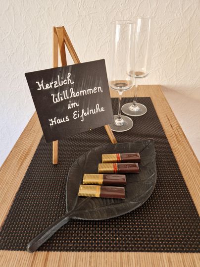 Un panneau de bienvenue est posé sur une table, entouré de flûtes de champagne. Sur une feuille se trouvent des barres chocolatées de différentes couleurs.