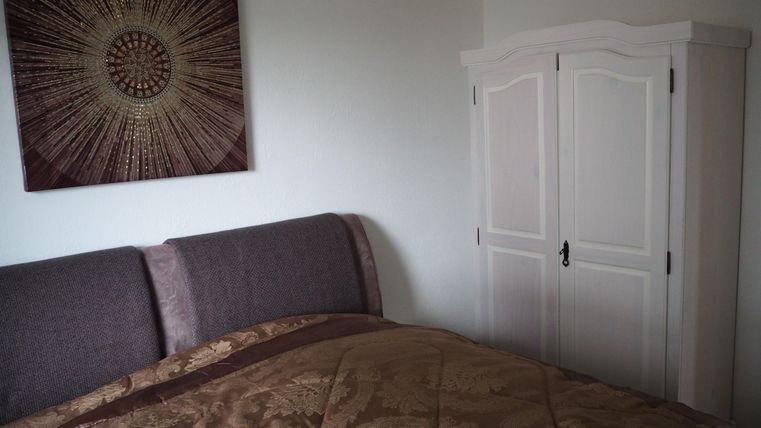 Ein modernes Schlafzimmer mit einem großen Bett und einer eleganten Bettdecke. An der Wand hängt ein dekoratives Kunstwerk, und in der Ecke steht ein weißer Schrank.