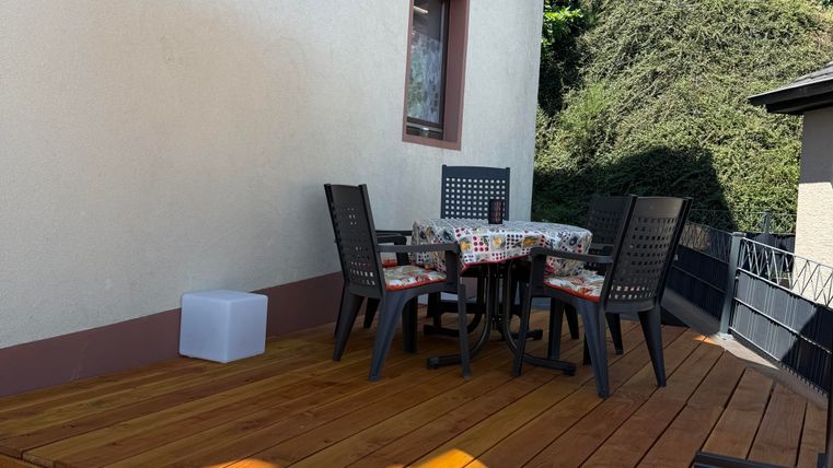 A cozy terrace with a wooden deck and a large sun umbrella. A round table with chairs invites you to linger.