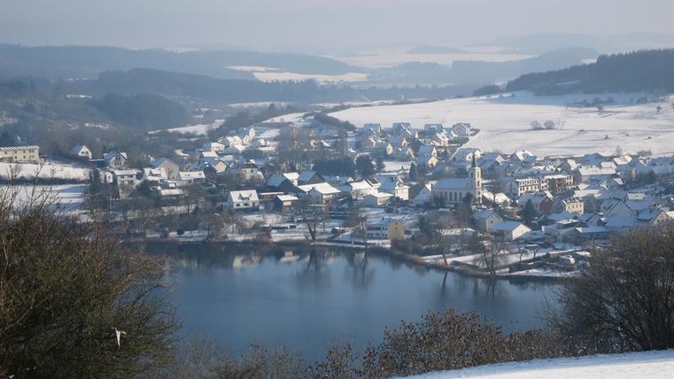 A picturesque village in winter with snow-covered roofs. A tranquil lake reflects the snowy landscape.
