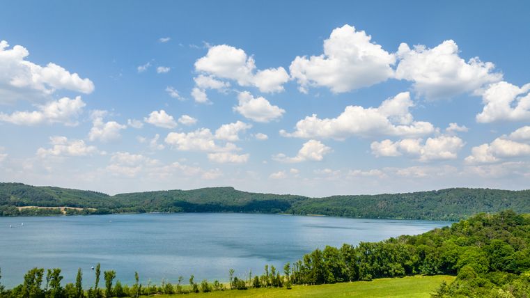 Eine große Wiese und der See mit bewaldeter Umgebung bei Sonnenschein