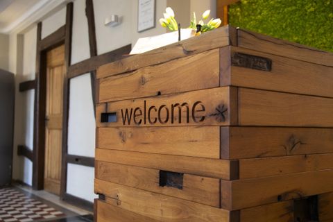 Een houten receptiebalie met de tekst "welcome". Op de achtergrond is een levendige plantenwand te zien.