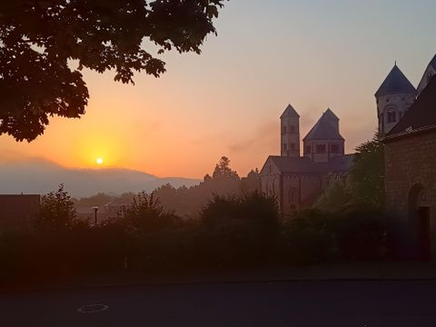 Un coucher de soleil pittoresque derrière une église historique. Les silhouettes des bâtiments sont entourées de douces collines et d'arbres.