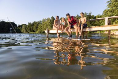 Eine Familie sitzt auf einem Steg am See