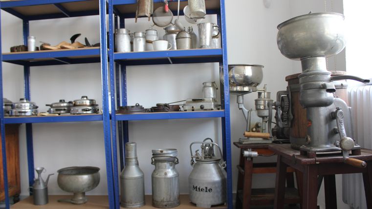 Une étagère avec divers anciens ustensiles et appareils de cuisine. Sur le côté droit se trouve une grande machine antique.