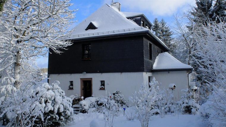 Ein wunderschönes Haus, umgeben von schneebedeckten Bäumen und Sträuchern. Der Himmel ist klar und blau.