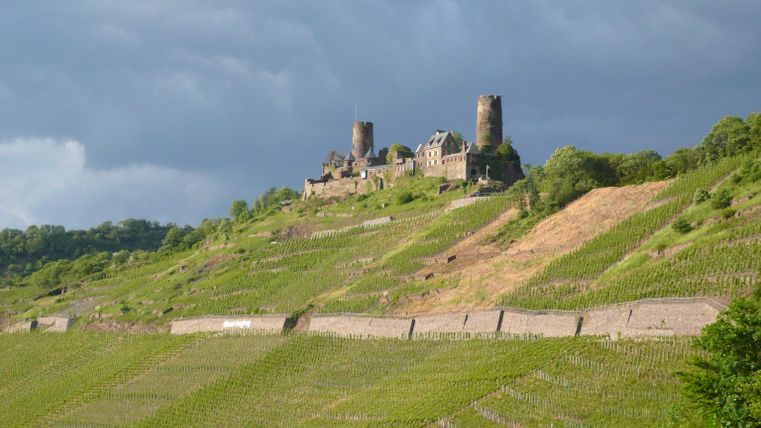 An old castle ruin rises on a green hill. Dark, overcast skies create a dramatic atmosphere.