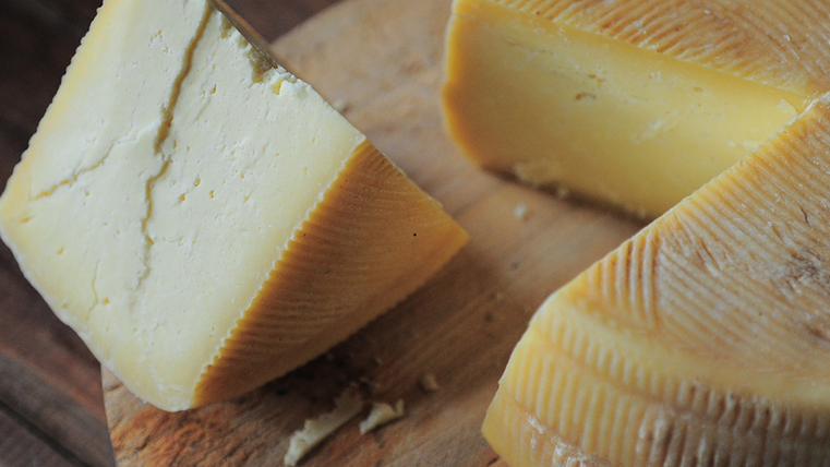 A large block of cheese has been cut and is resting on a wooden tray.