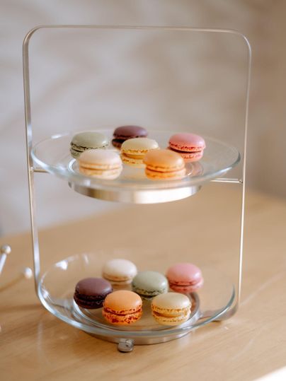 A stylish tiered stand with colorful macarons in various flavors. The macarons are arranged on two levels, providing an appealing presentation.