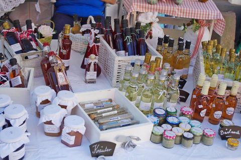 Un stand de marché coloré avec différentes bouteilles et bocaux remplis de confitures et de boissons. Les produits sont joliment emballés et étiquetés.