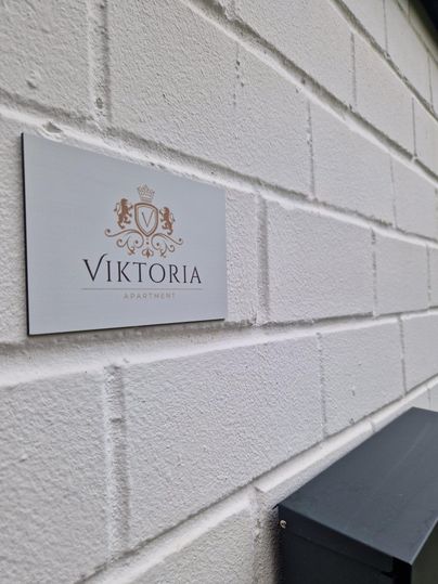 Ein Schild mit der Aufschrift "VIKTORIA" an einer weißen Wand. Daneben befindet sich ein grauer Briefkasten.