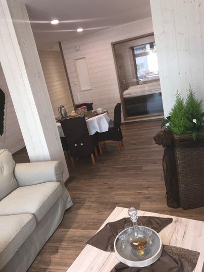 An inviting living room with a comfortable sofa and a table in the dining area. The room has bright walls and a warm wooden floor, creating a cozy atmosphere.