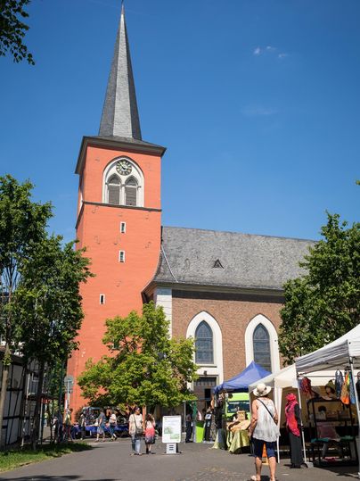 Een prachtige kerk met een hoge, spitse toren staat op de achtergrond. Voor de kerk vindt een markt met kraampjes plaats.