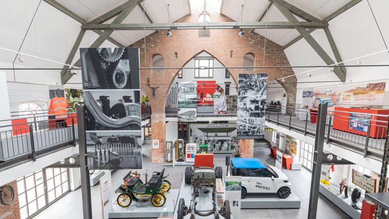 Ein modernes Museum mit historischen Fahrzeugen und großen Wandbildern. Der Raum hat hohe Decken und eine offene Architektur.
