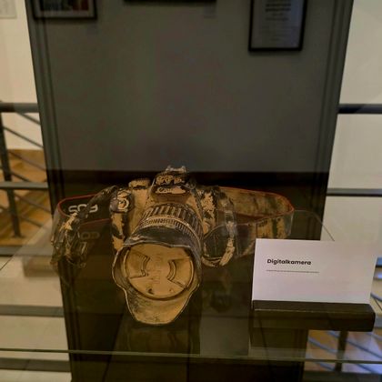 Een oude camera in een vitrine. Daarnaast bevindt zich een bord met de beschrijving van het object.