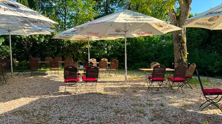 A cozy outdoor area with seating and umbrellas. The surroundings are green and inviting.