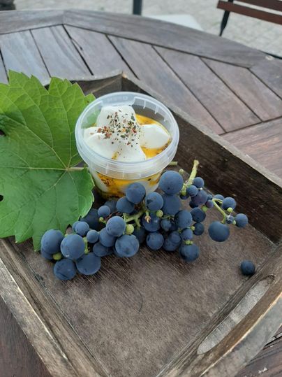 Ein Dessert in einer Kunststoffschale mit Sahne und Gewürzen. Daneben liegen frische, dunkle Trauben und ein Blatt.